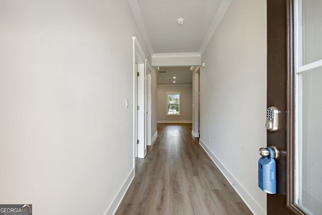 hallway with ornamental molding, visible vents, light wood-style flooring, and baseboards