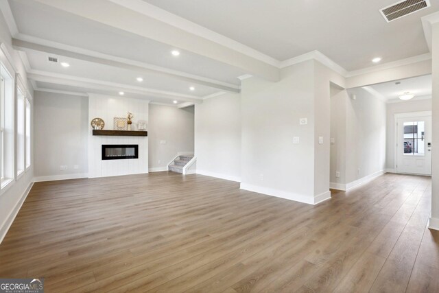 unfurnished living room with visible vents, wood finished floors, beamed ceiling, crown molding, and a fireplace