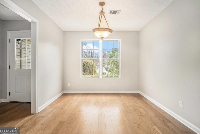 unfurnished dining area featuring a textured ceiling, light wood-style flooring, visible vents, and baseboards