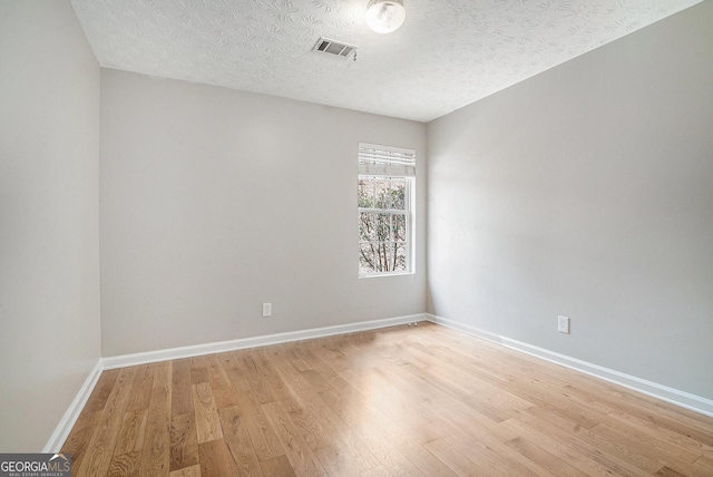 empty room featuring visible vents, light wood-style flooring, baseboards, and a textured ceiling