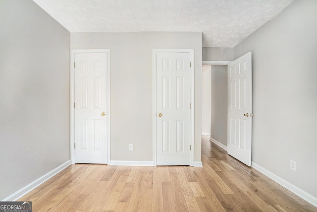 unfurnished bedroom featuring light wood-style floors, a textured ceiling, and baseboards