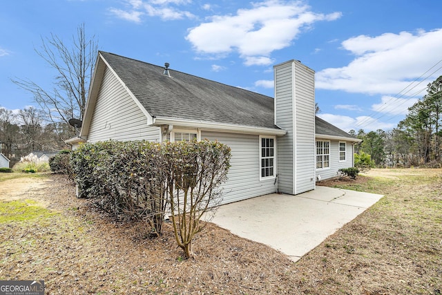 back of house with a patio area, a chimney, and roof with shingles