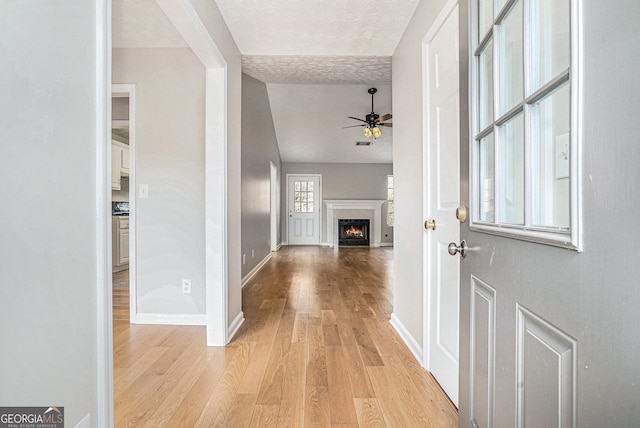 entrance foyer with a warm lit fireplace, baseboards, a ceiling fan, a textured ceiling, and light wood-style floors