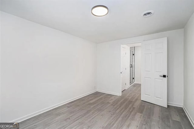 spare room with wood finished floors, visible vents, and baseboards