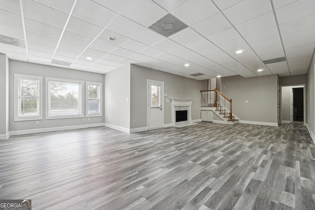 unfurnished living room with a paneled ceiling, a fireplace, wood finished floors, baseboards, and stairway