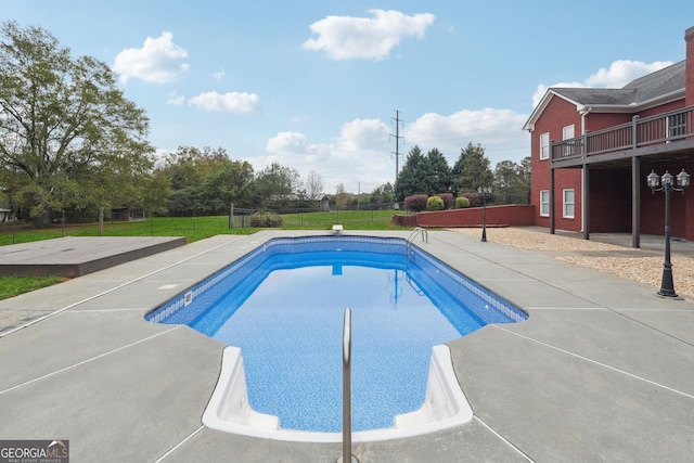 outdoor pool with a patio, fence, and a lawn