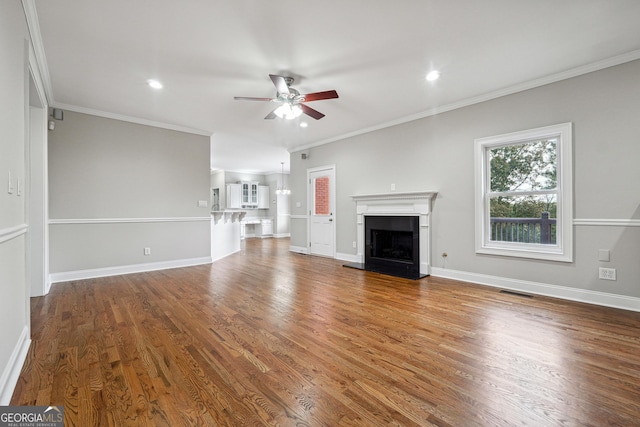 unfurnished living room featuring a fireplace with raised hearth, ceiling fan, wood finished floors, baseboards, and ornamental molding