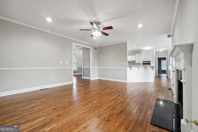 unfurnished living room with baseboards, a ceiling fan, wood finished floors, and ornamental molding