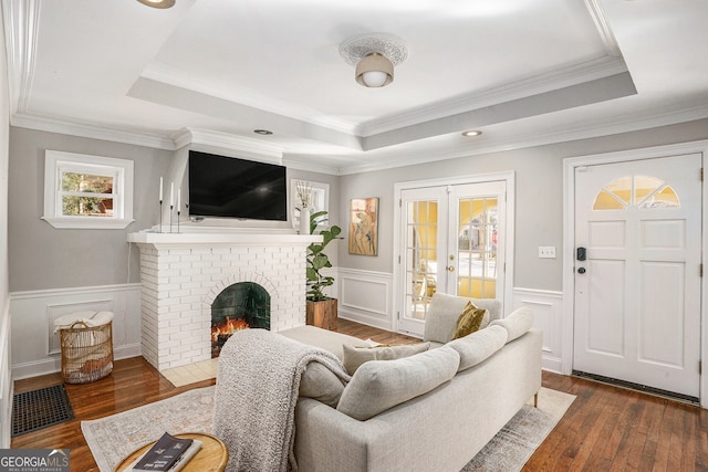 living room featuring a brick fireplace, a tray ceiling, dark wood-style flooring, and french doors