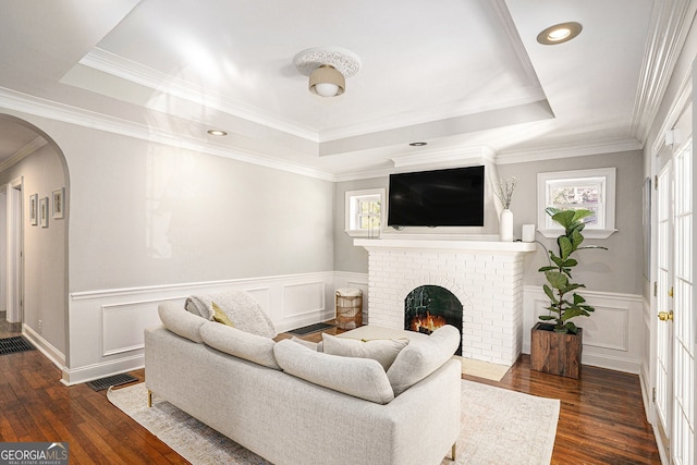 living room with dark wood-style floors, arched walkways, a raised ceiling, and a fireplace