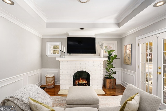 living area featuring a tray ceiling, a brick fireplace, french doors, and wood finished floors
