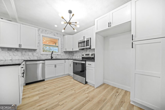 kitchen with white cabinetry, light wood-style floors, appliances with stainless steel finishes, dark countertops, and an inviting chandelier