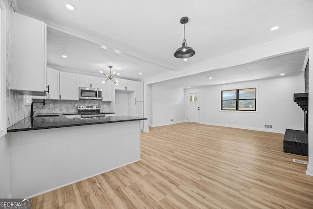 kitchen with light wood finished floors, stainless steel appliances, white cabinets, a sink, and a peninsula