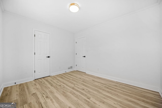 spare room with light wood-style floors, visible vents, crown molding, and baseboards