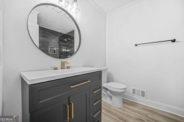 bathroom featuring visible vents, toilet, ornamental molding, vanity, and wood finished floors