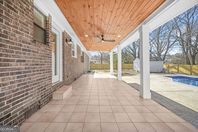 view of patio featuring a storage shed, ceiling fan, an outdoor structure, and a fenced backyard