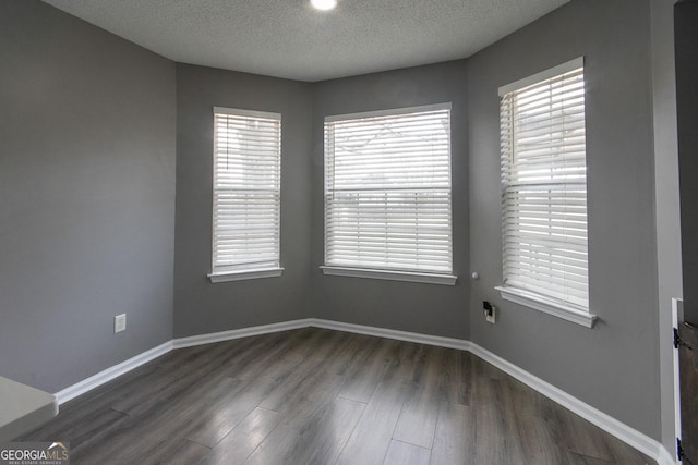 spare room featuring dark wood-style floors, a textured ceiling, and baseboards