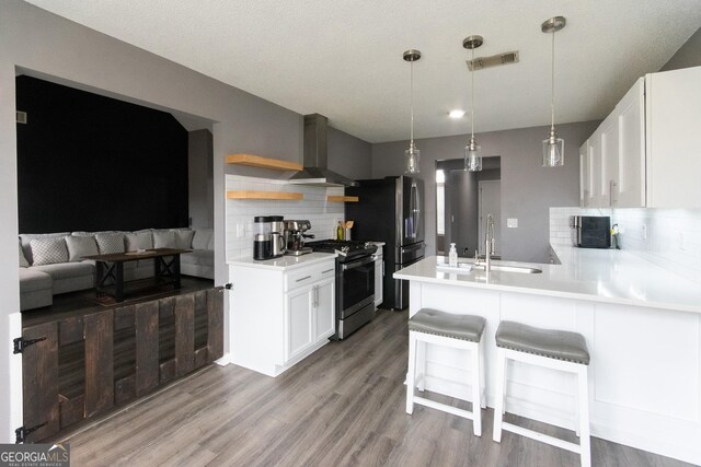 kitchen featuring stainless steel appliances, a peninsula, a sink, visible vents, and wall chimney exhaust hood