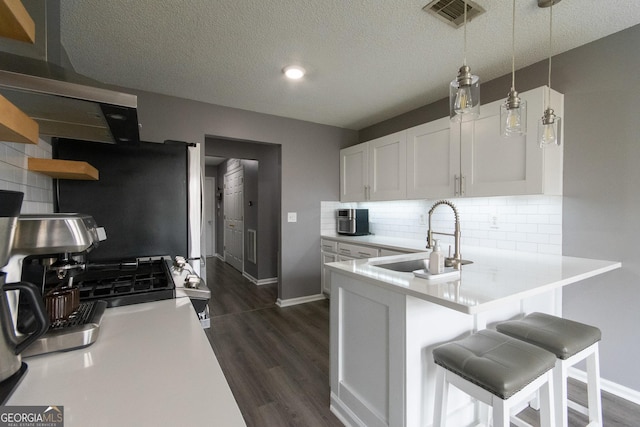 kitchen featuring dark wood-style flooring, light countertops, visible vents, decorative backsplash, and a sink