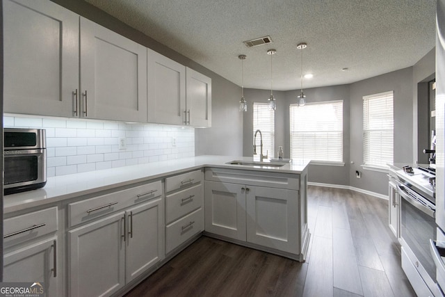 kitchen with a peninsula, dark wood-type flooring, a sink, stainless steel range with electric cooktop, and light countertops