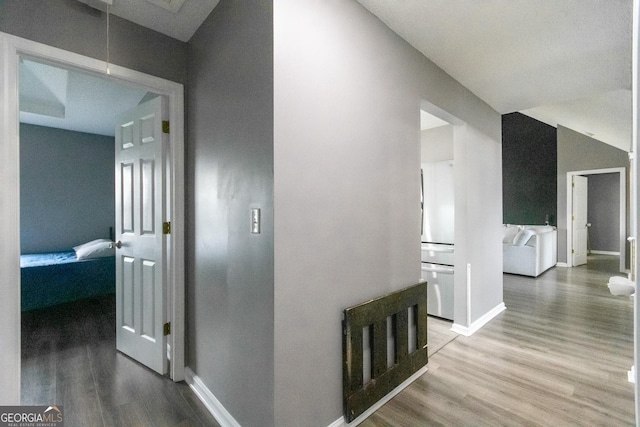 hallway with attic access, lofted ceiling, baseboards, and wood finished floors