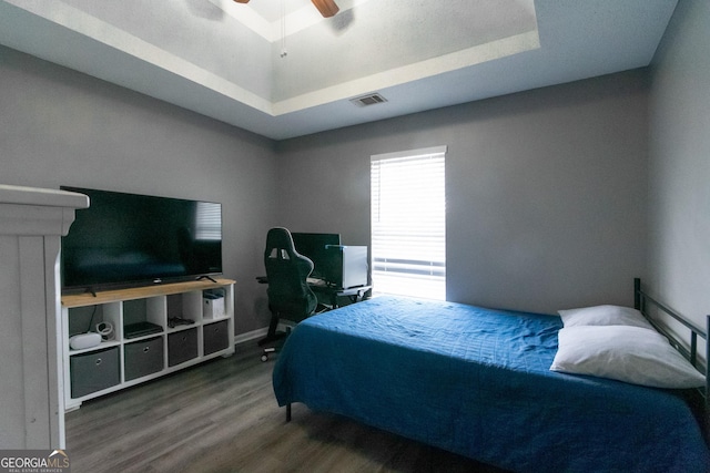 bedroom featuring a ceiling fan, visible vents, a raised ceiling, and wood finished floors