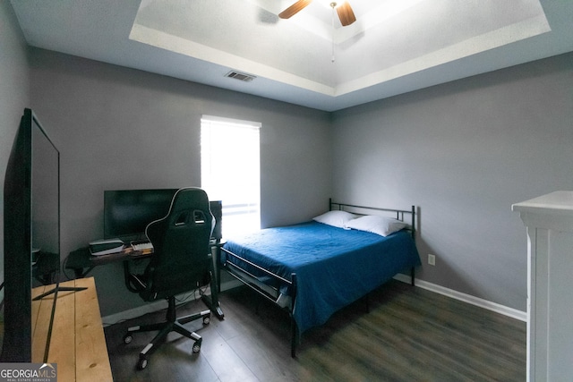 bedroom featuring a tray ceiling, visible vents, and wood finished floors