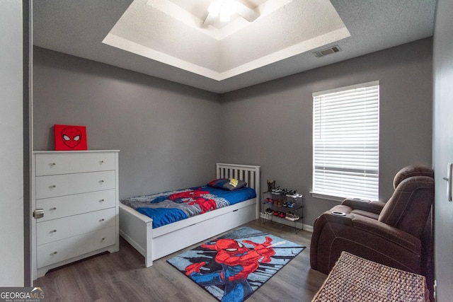 bedroom with a tray ceiling, visible vents, a textured ceiling, and wood finished floors