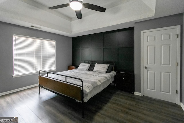 bedroom featuring visible vents, a raised ceiling, dark wood-style flooring, and a decorative wall