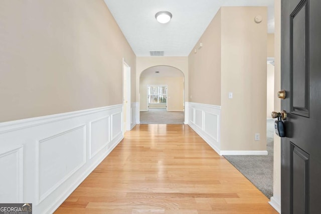 corridor with arched walkways, wainscoting, visible vents, and a decorative wall