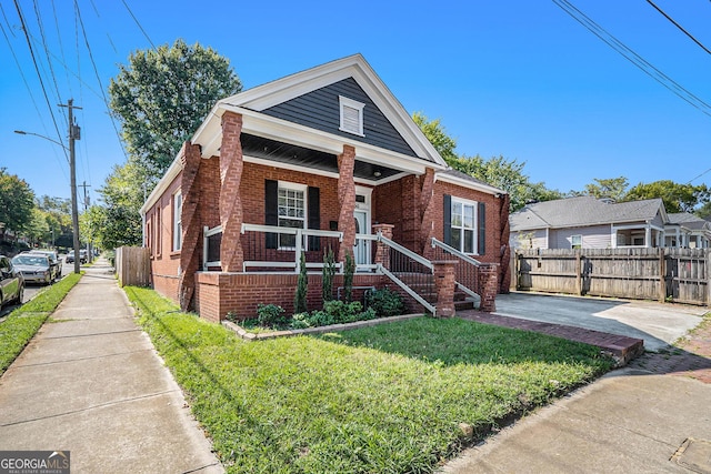 bungalow-style home featuring brick siding, covered porch, a front lawn, and fence