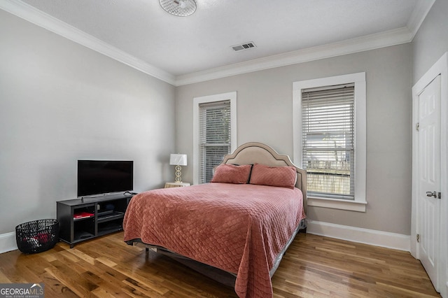 bedroom with visible vents, crown molding, baseboards, and wood finished floors