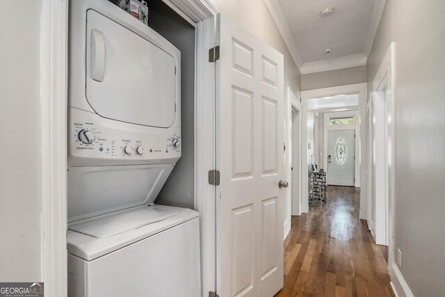 clothes washing area with crown molding, wood finished floors, laundry area, and stacked washing maching and dryer