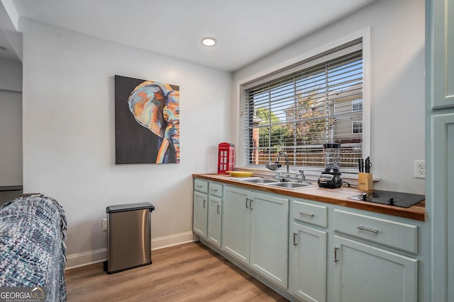 kitchen with a sink, baseboards, light wood finished floors, black electric cooktop, and wooden counters