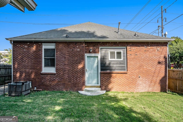 rear view of property with brick siding, a shingled roof, fence, cooling unit, and a yard