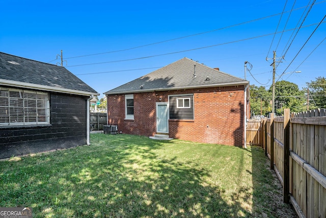 back of property with central air condition unit, a lawn, brick siding, and a fenced backyard