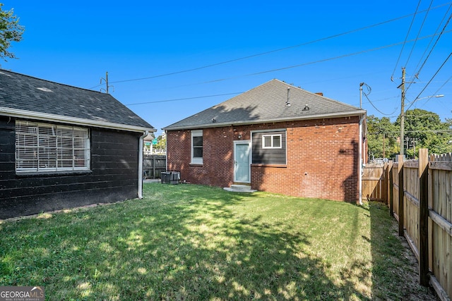 back of house featuring a yard, a fenced backyard, central AC, a shingled roof, and brick siding