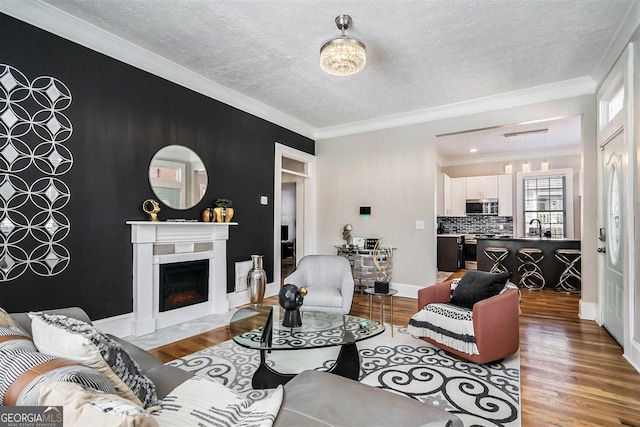 living room featuring a textured ceiling, wood finished floors, a warm lit fireplace, and ornamental molding