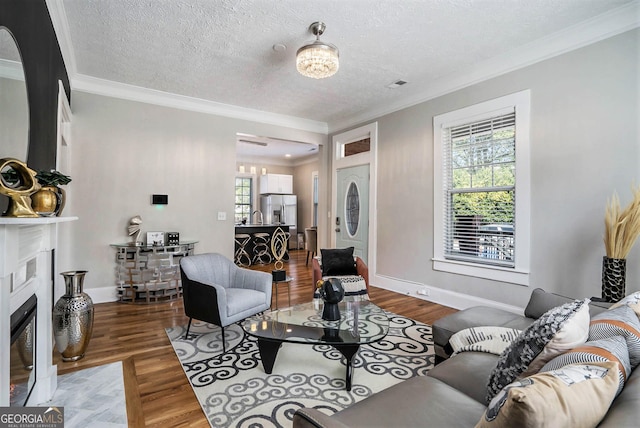 living area with a fireplace with flush hearth, a textured ceiling, wood finished floors, crown molding, and baseboards