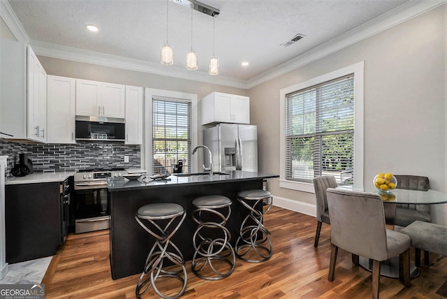 kitchen with a sink, appliances with stainless steel finishes, wood finished floors, and ornamental molding