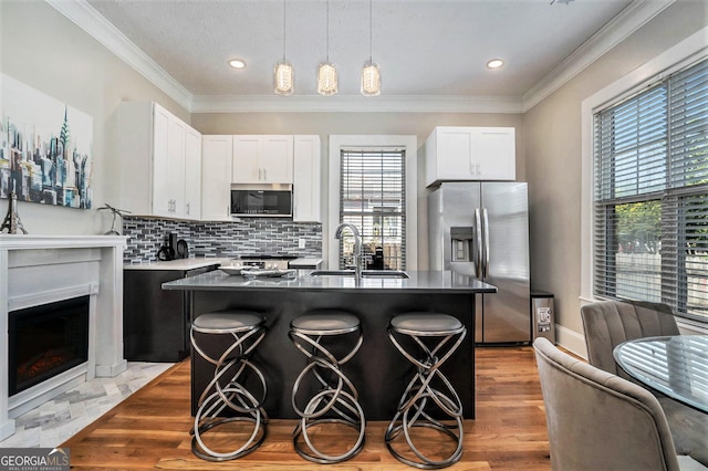 kitchen with a sink, dark countertops, stainless steel appliances, a breakfast bar area, and crown molding