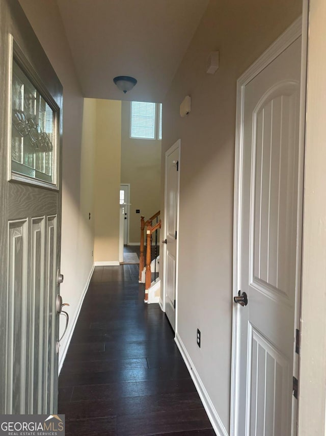 hallway featuring dark wood finished floors, a towering ceiling, baseboards, and stairs