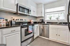 kitchen featuring stainless steel appliances, dark countertops, a sink, and white cabinets