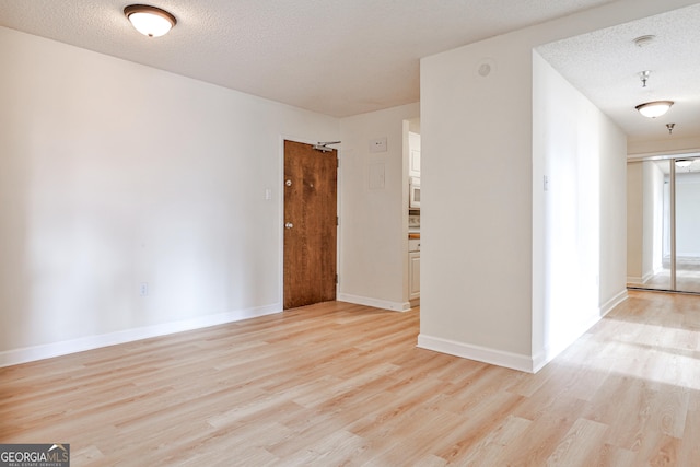 spare room with baseboards, light wood-style flooring, and a textured ceiling