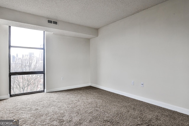 carpeted spare room featuring a textured ceiling, visible vents, and baseboards