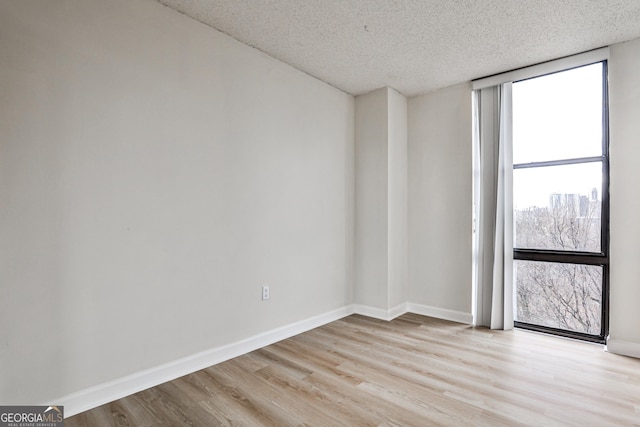 empty room with a textured ceiling, light wood-type flooring, and baseboards