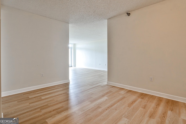 empty room featuring light wood-style flooring, baseboards, and a textured ceiling