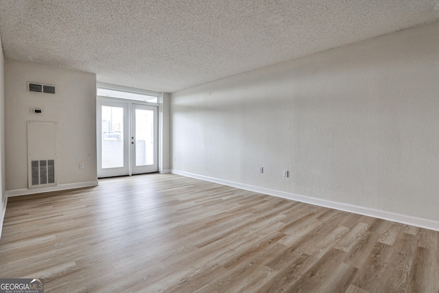 empty room featuring french doors, visible vents, light wood-style flooring, and a textured ceiling