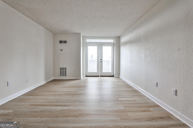 foyer featuring a textured wall, french doors, light wood-type flooring, and visible vents