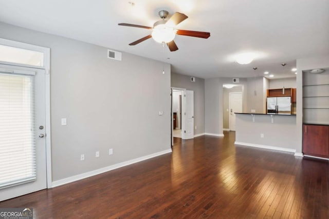 unfurnished living room featuring dark wood-style floors, a ceiling fan, visible vents, and baseboards